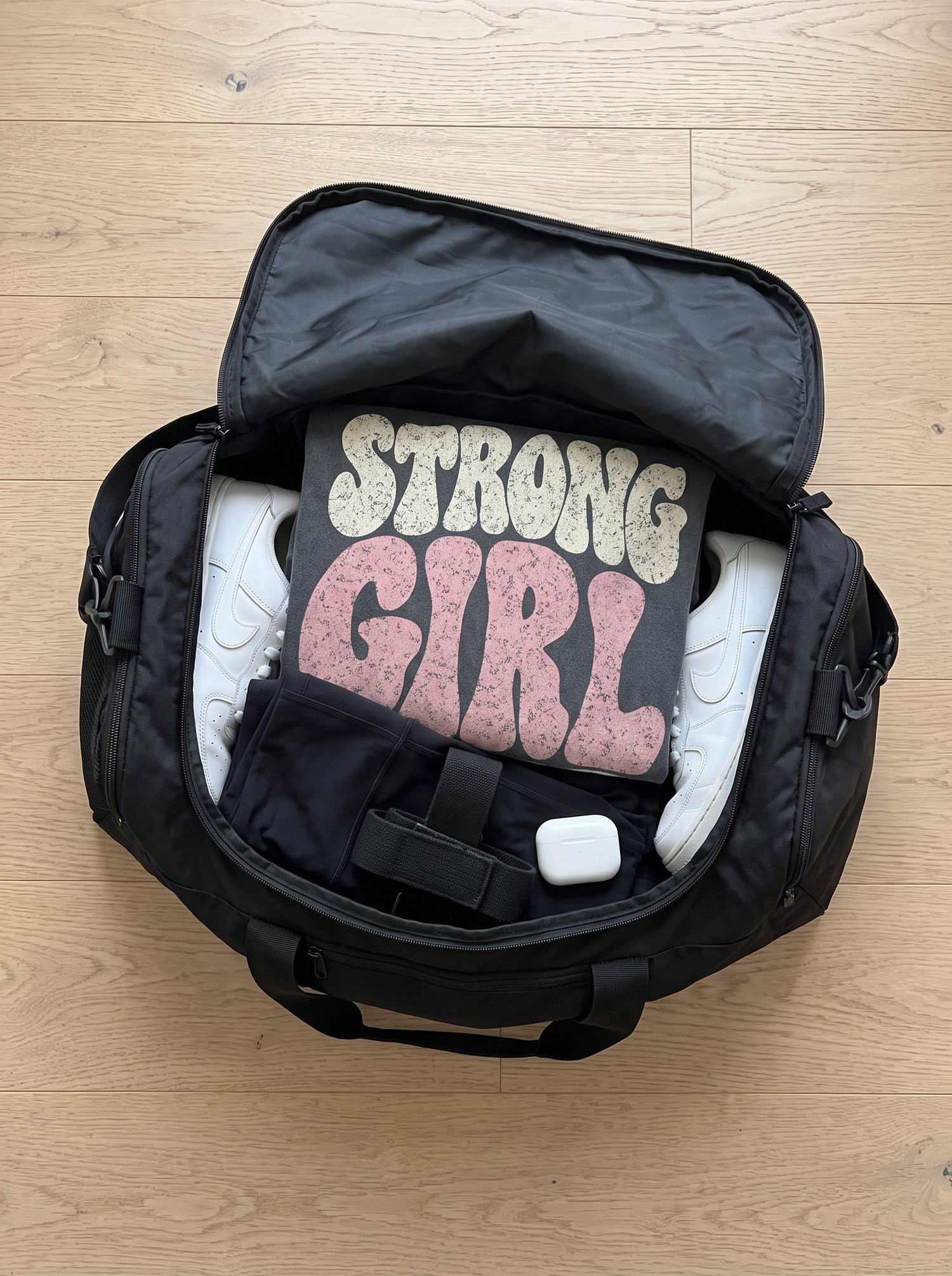 Open gym bag packed with an oversized tee, sneakers and straps