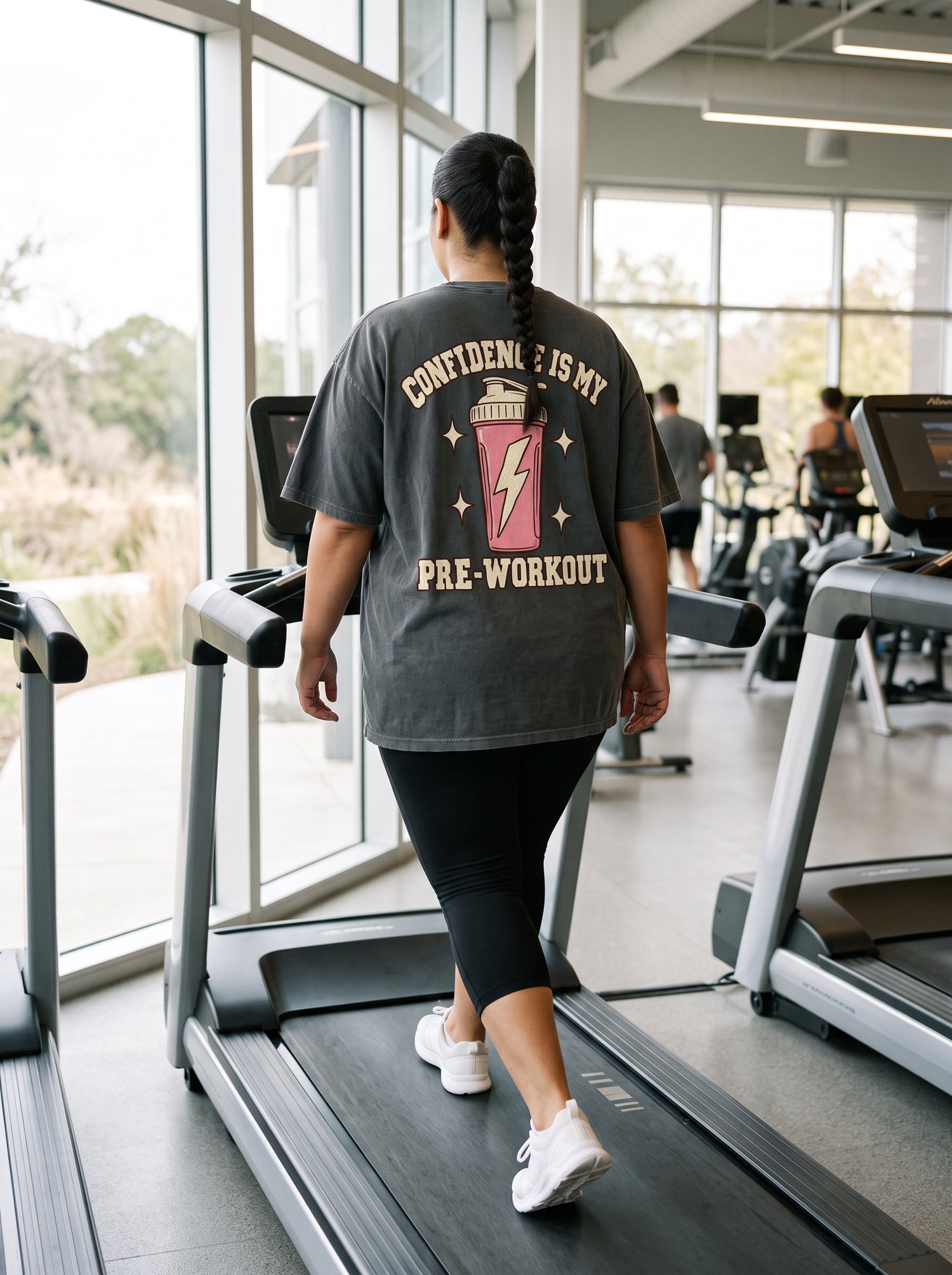 Woman walking on a treadmill wearing an oversized Confidence Is My Pre-Workout tee and capri leggings