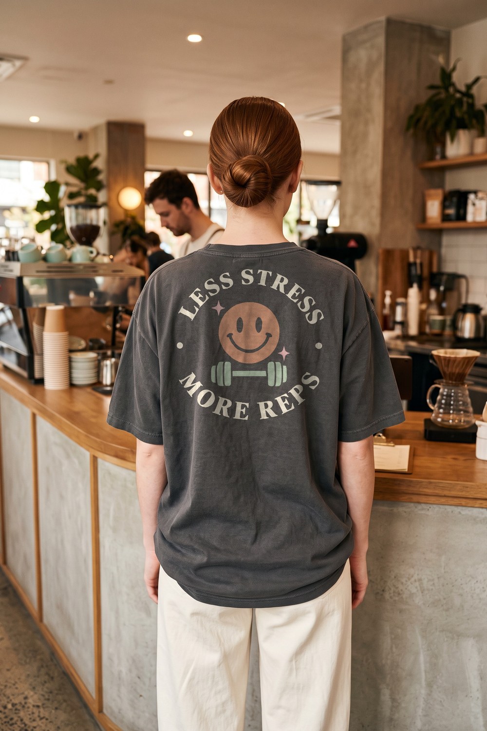 Woman at a coffee bar in a Less Stress More Reps oversized tee