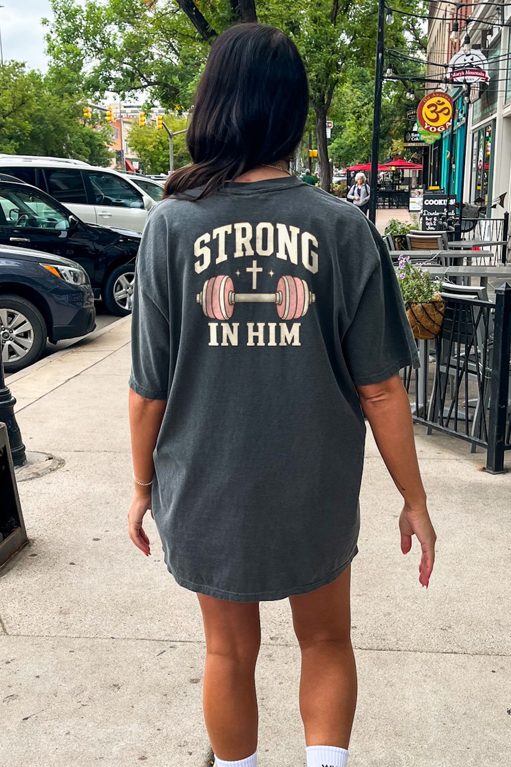 Woman walking down the street in an oversized Strong In Him tee in Pepper